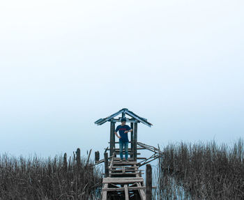 Man standing on weathered footbridge by lake against sky