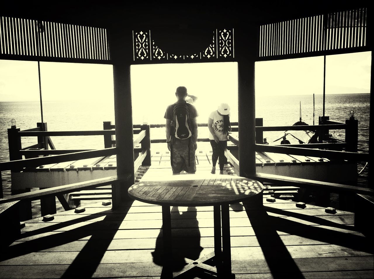 railing, lifestyles, sea, leisure activity, men, person, standing, rear view, indoors, built structure, water, pier, sitting, horizon over water, architecture, sky, full length