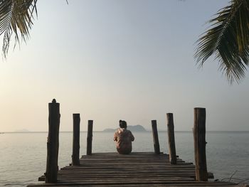 Rear view of woman sitting on pier over sea against sky