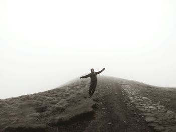 Man with arms outstretched standing on mountain against sky during foggy weather