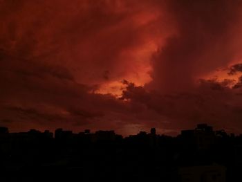 Silhouette of city against dramatic sky at sunset