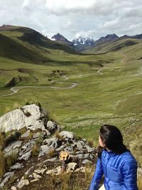 Woman sitting on rock by landscape against cloudy sky