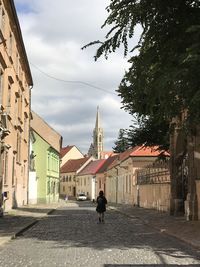 Man walking on street amidst buildings against sky in city