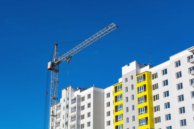 Low angle view of crane by building against clear blue sky