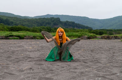 Woman playing with sand at beach against sky