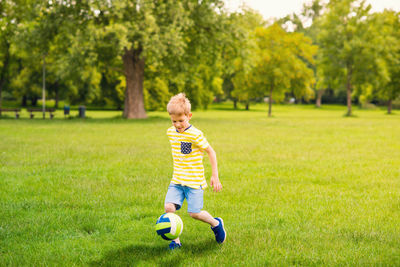 Full length of boy playing on soccer field against trees