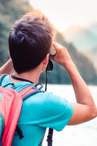 Young tourist with backpack looks through a binoculars on mountains peaks
