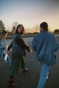 Rear view of friends on beach against sky during sunset