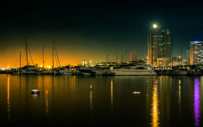 Illuminated cityscape by sea against sky at night