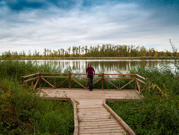 Rear view of person on footbridge over lake against sky