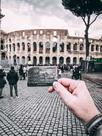 Cropped hand of man holding photograph against historical building