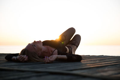 Sensuous woman lying on pier over sea against sky during sunset