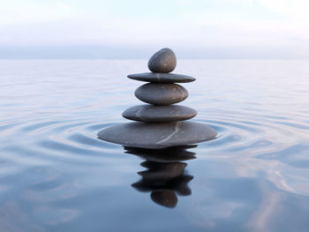 Stack of stones in sea against sky