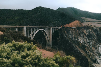 Arch bridge by mountains against sky