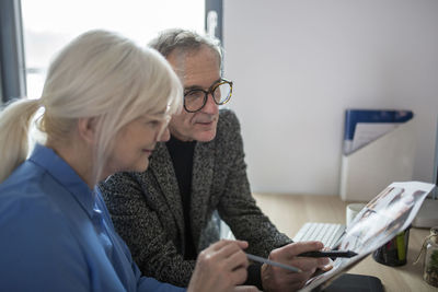 Two senior colleagues working together at desk in office examining photos