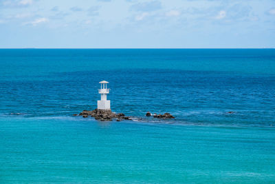 Lighthouse by sea against blue sky