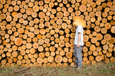 Side view of man standing against log stacks