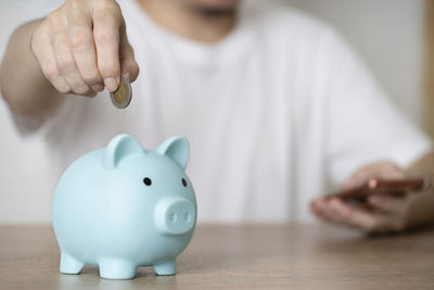 Midsection of man putting coin in piggy bank