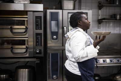 Side view of chef carrying plate while walking in commercial kitchen