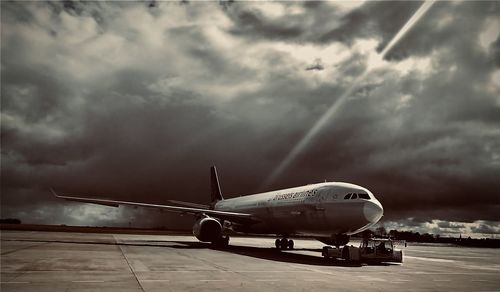 Airplane on airport runway against cloudy sky