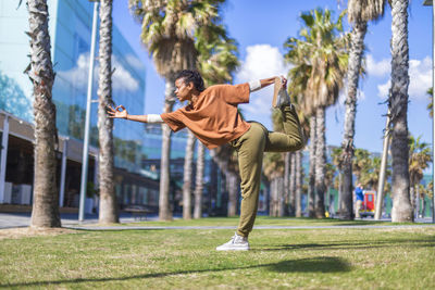 Full length of woman exercising while standing grass against sky