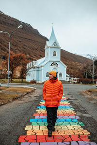 Young tourist walking on street between buildings of village near cathedral and mountain