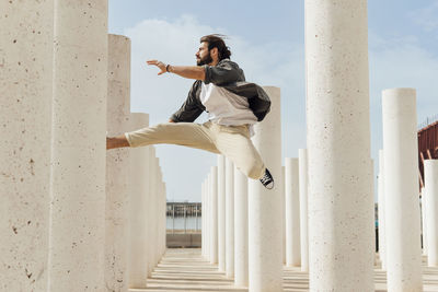 Carefree young man jumping between white columns on sunny day