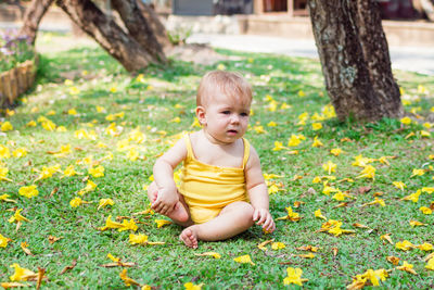 Adorable baby girl with blond hair is playing on grass with yellow flowers. 