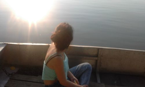 Rear view of woman sitting on railing against bright sun