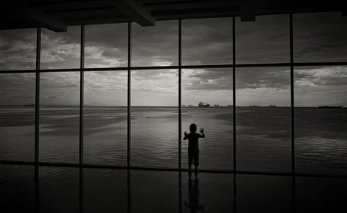 Silhouette man photographing sea seen through window