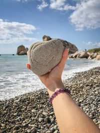 Cropped hand of woman holding rock at beach against sky