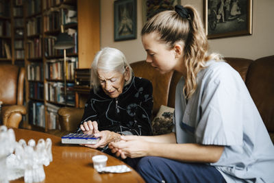 Senior woman talking with female caregiver over medicine box in living room