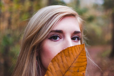 Close-up portrait of young woman holding autumn leaf at forest