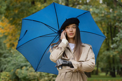 Cyber woman under an umbrella with a bionic prosthesis on her arm is talking on the phone and