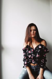 Portrait of beautiful woman sitting against wall