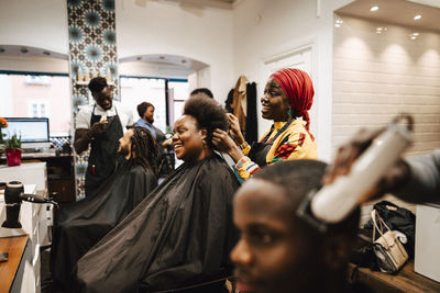 Multiracial hair expertise making hairstyle of male and female customers at barber shop