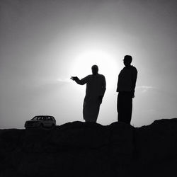 Silhouette men standing on rock against clear sky