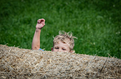 High angle view of boy with hand raised by hay bale