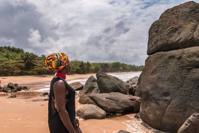 African woman standing on a beautiful beach with dark big stones and clean beach