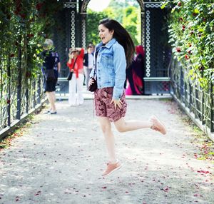 Cheerful woman jumping in mid-air on pathway amidst plants at park