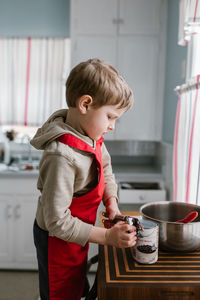 Side view of cute boy opening canned food on table at home