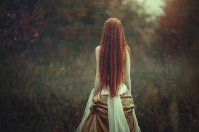 Rear view of woman standing against trees in forest
