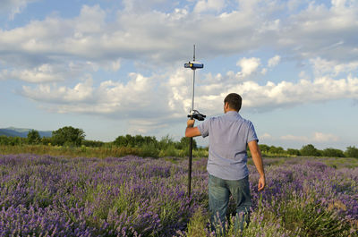 Rear view of surveyor with theodolite on lavender field against sky