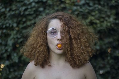 Portrait of shirtless woman with fruit in mouth 