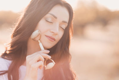 Woman making massage with facial stone roller over sunny nature background closeup. 