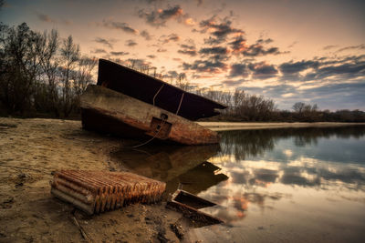 Abandoned boat moored on lake against sky during sunset
