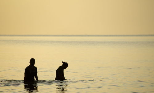 Silhouette people on sea against sky during sunset