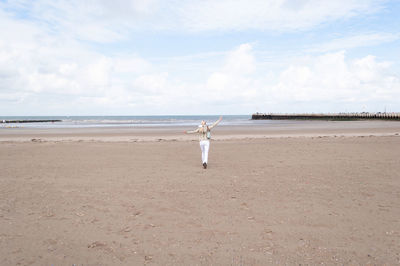 Tiny woman runs open arms along the beach to the sea