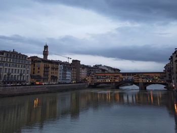 Bridge over river by buildings against sky at dusk