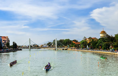 People on bridge over river against sky in city